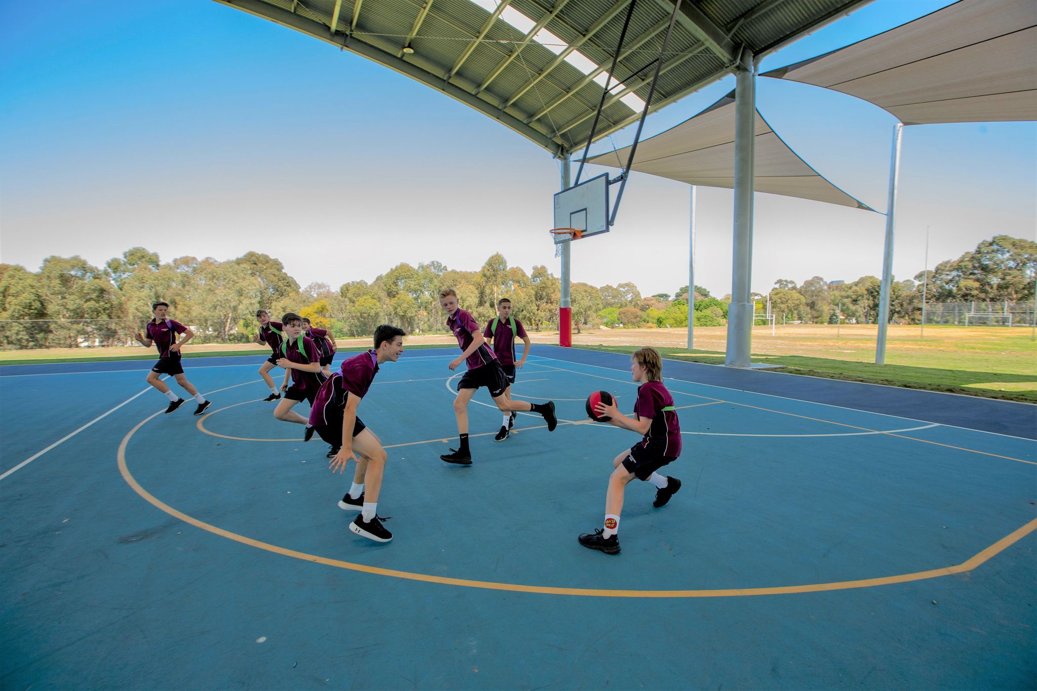 School students playing basketball on an outdoor blue acrylic court