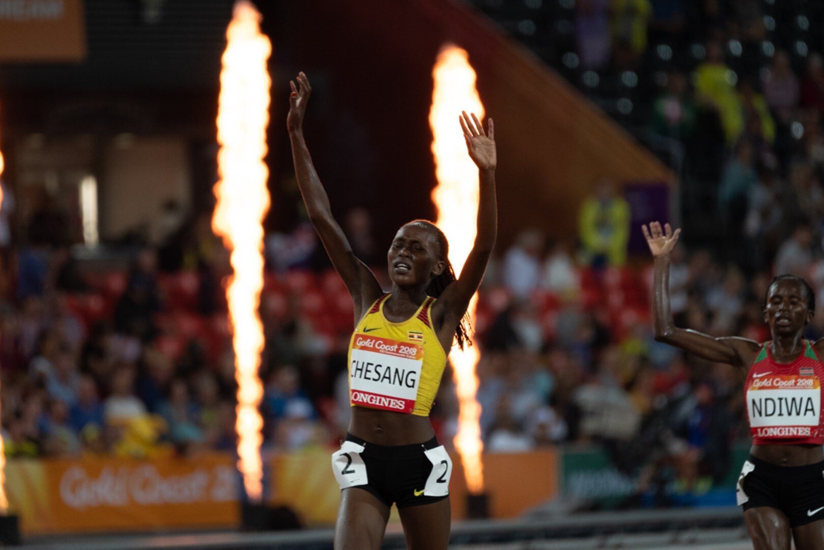 Black woman running raising her hands on running track 